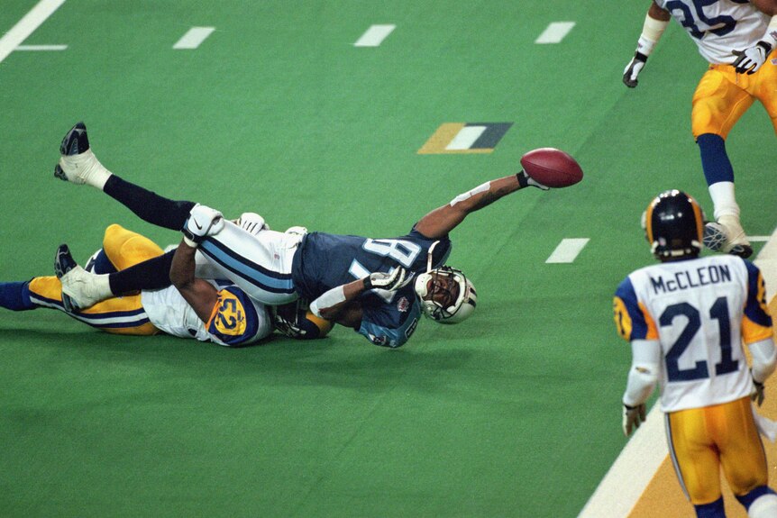 An NFL player stretches out his arm while tackled but the ball he's holding is less than a yard from the end zone.