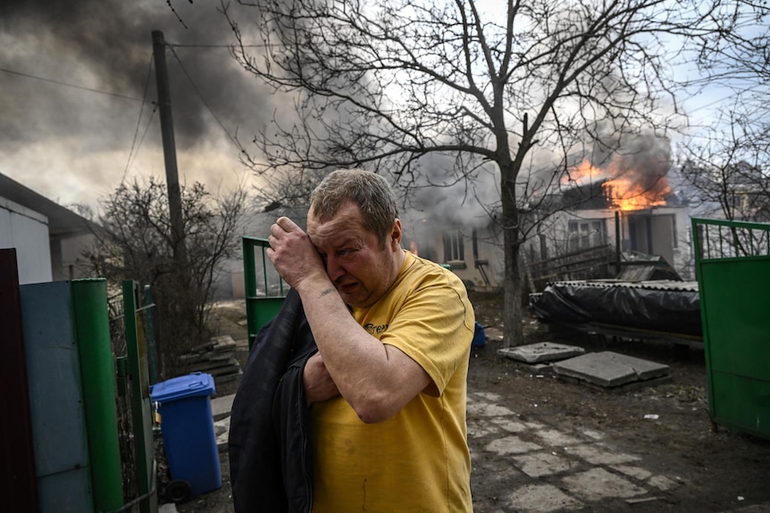 A man wipes away tears as he cries in front of his burning home.