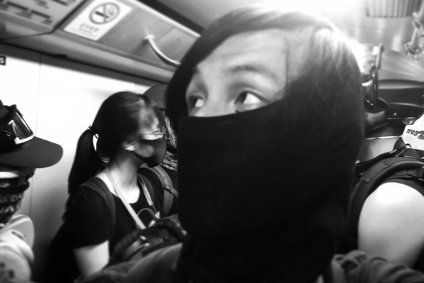 Black and white photo of protestor with face half covered on train.