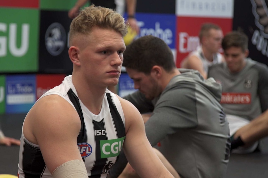 Football player sitting in a changeroom looking sad.