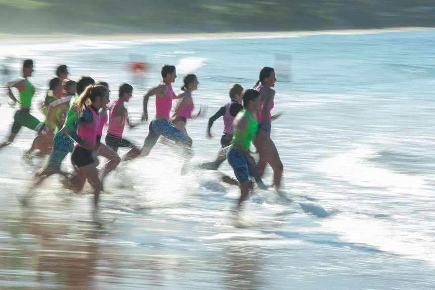 A large group of young lifesavers sprint frenetically into the water