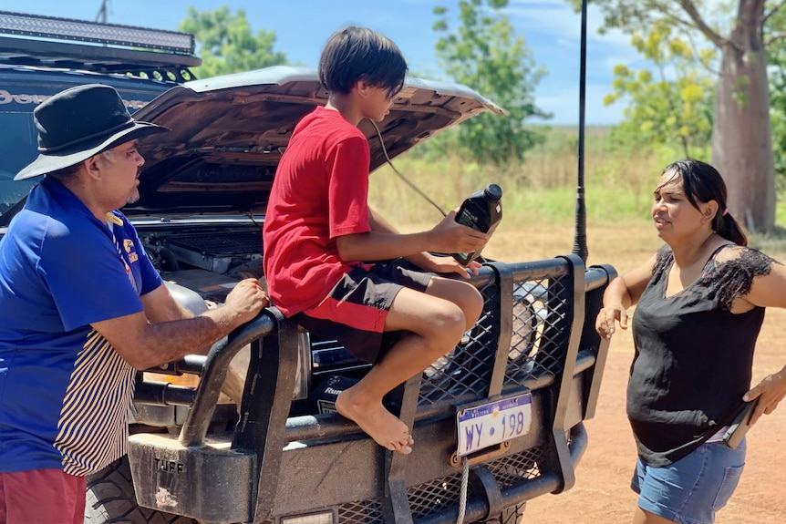 A man and a woman stand beside a four-wheel drive, with a child sitting on the bullbar.