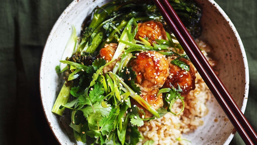 A bowl of brown rice topped with sticky pork meatballs, broccolini, coriander, spring onions, an Asian-inspired dinner recipe.