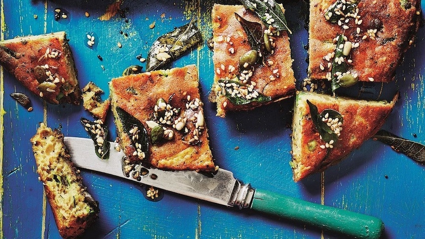 Savoury zucchini seed and curry leaf cake cut in slices, knife on table.