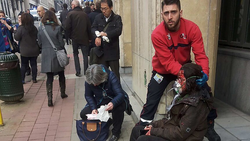 A security guard assists an injured woman on the steps outside a building in Brussels.