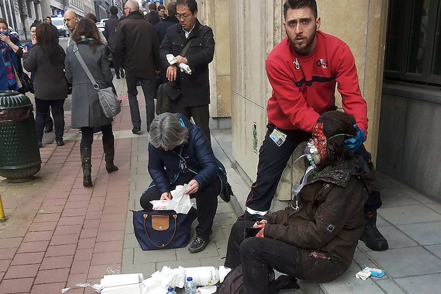 A security guard assists an injured woman on the steps outside a building in Brussels.