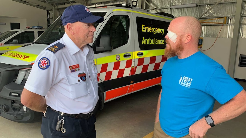Two men talk in front of an ambulance.