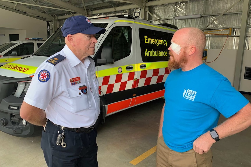 Two men talk in front of an ambulance.