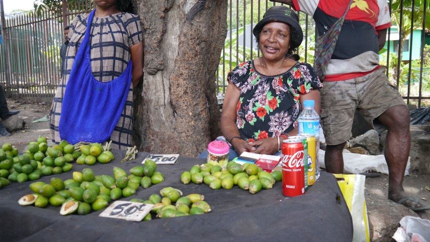 Woman in Papua New Guinea sits at street side table with groupings of green looking fruit, betel nut, for sale.  