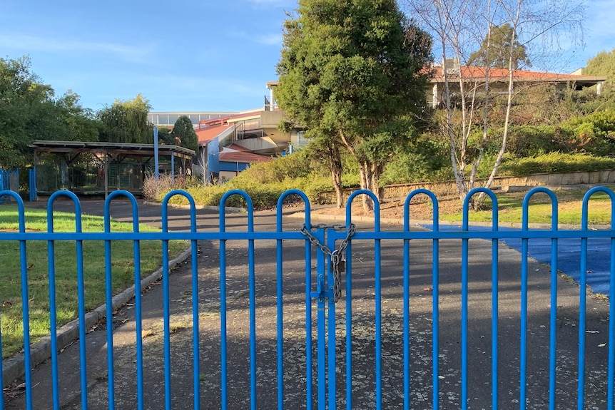 A locked blue gate and padlock in front of an old school campus.