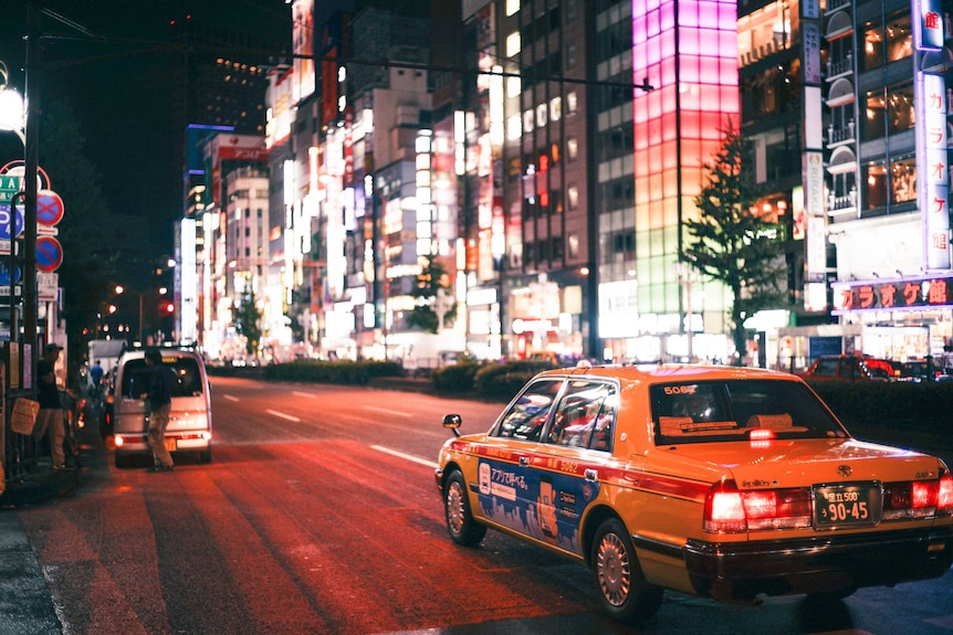 A cab drives down a street in the Shinjuku district of Tokyo at night.