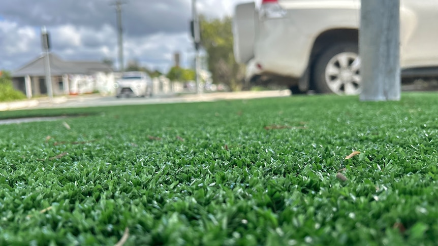 An image of green artificial turf with a white car driving by in the distance.