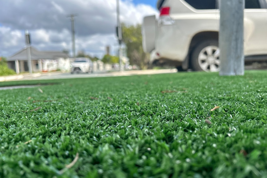 An image of green artificial turf with a white car driving by in the distance.