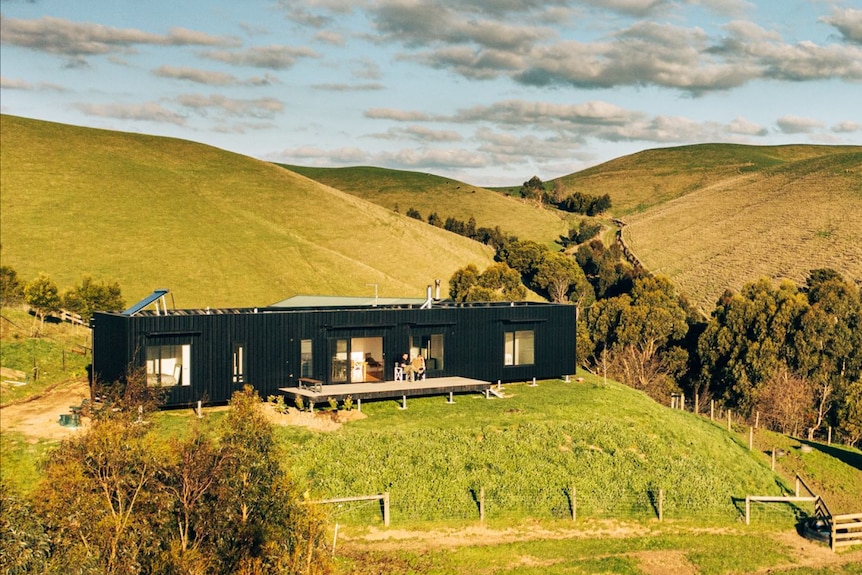 A rectangular black house house sitting on top of a hill in the country.