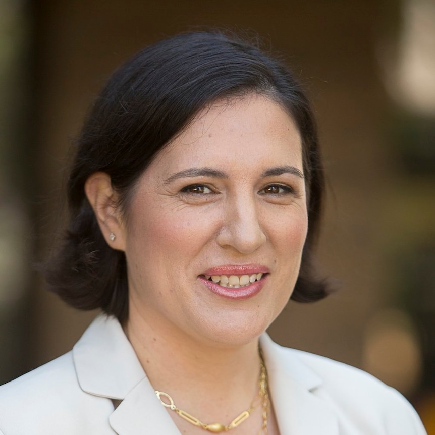 Katina Michael is a professor who studies information technology and computing, she is wearing a white blazer and smiling.