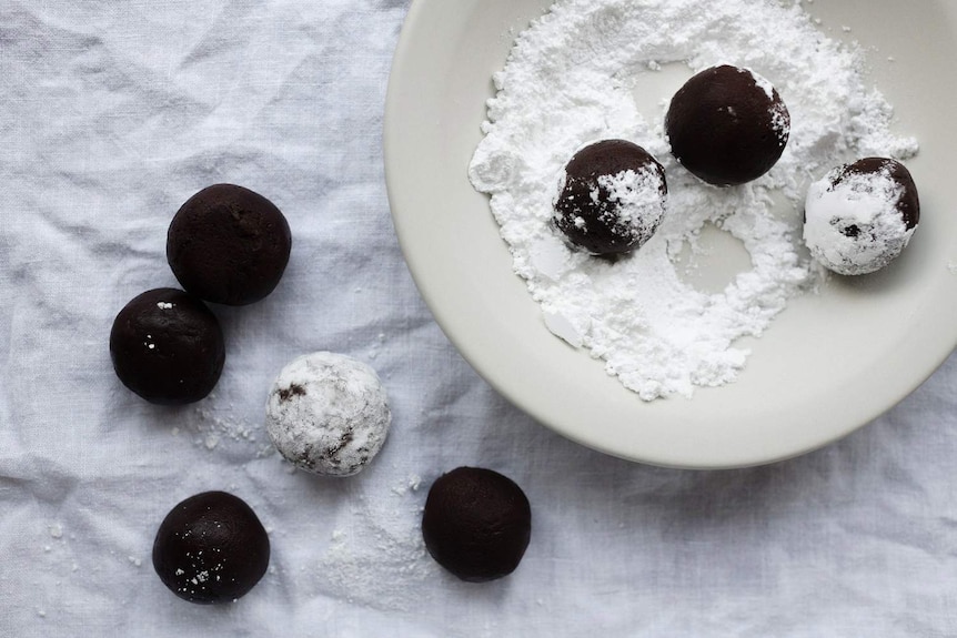 Dark chocolate crinkle cookie dough balls being rolled in icing sugar.
