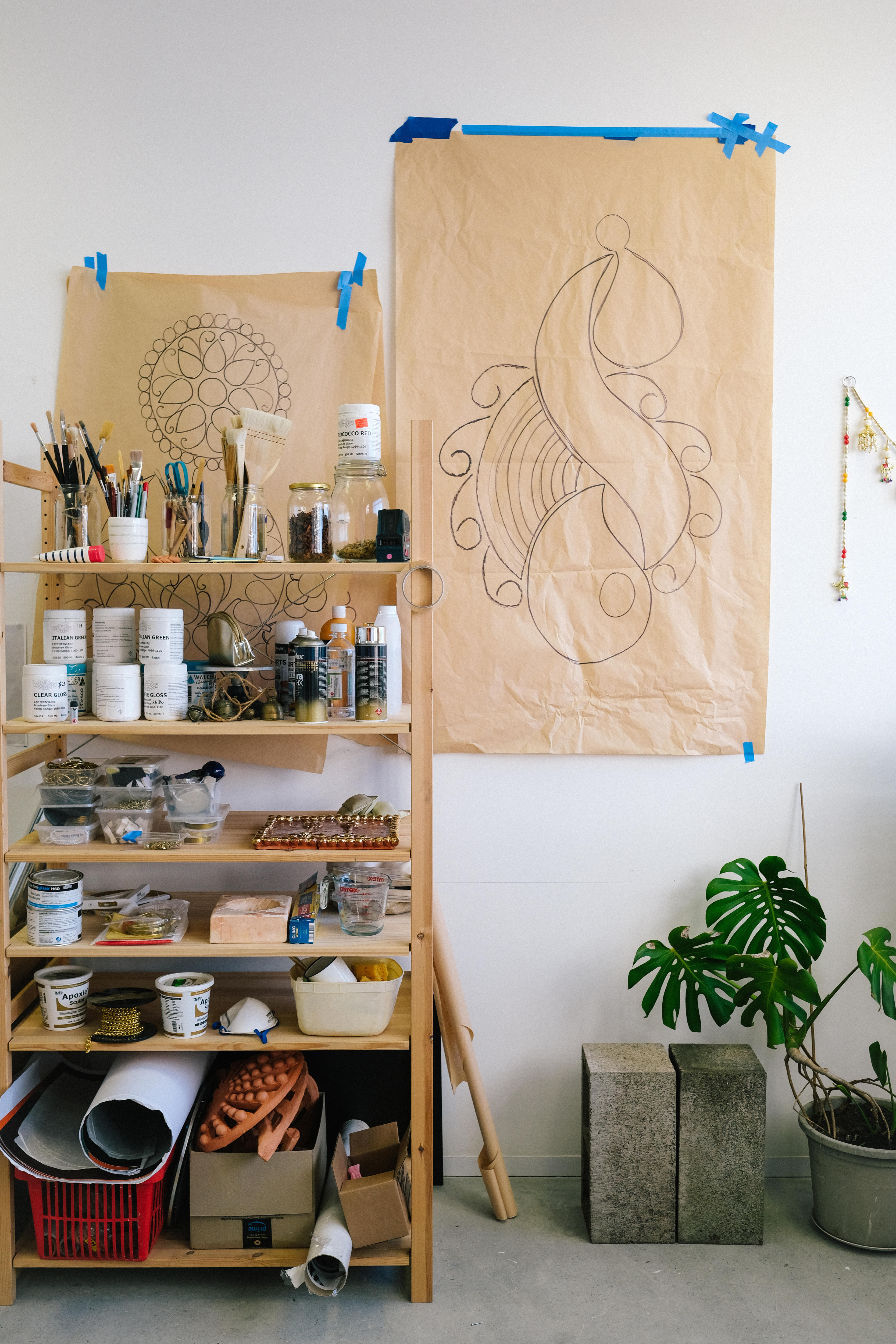 Large earring sketches on brown paper stuck on the studio wall, next to shelving containing art supplies.