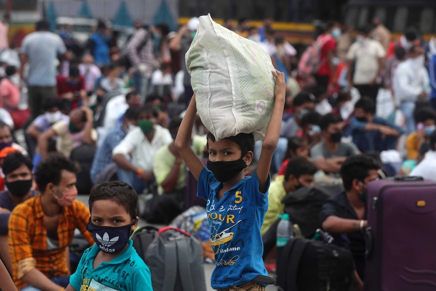 Small children wearing facemasks wait in a large crowd wait for a train.