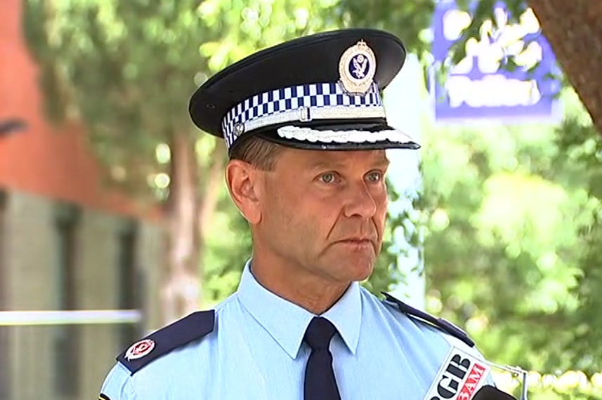 A police officer speaking to journalists in front of a station.