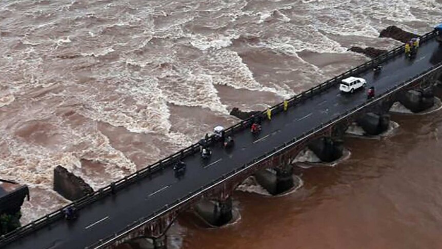 A partially collapsed road bridge in raging flood waters.
