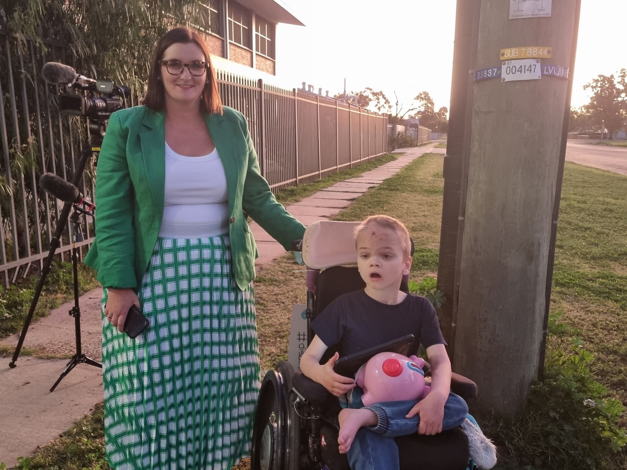 A boy in a wheelchair sitting next to a woman standing and smiling