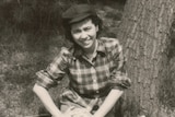 A black and white photo of a woman in a check shirt and black cap. 