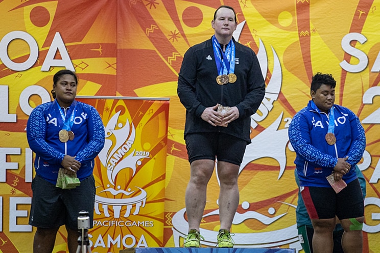 Three women weightlifters stand on a podium.