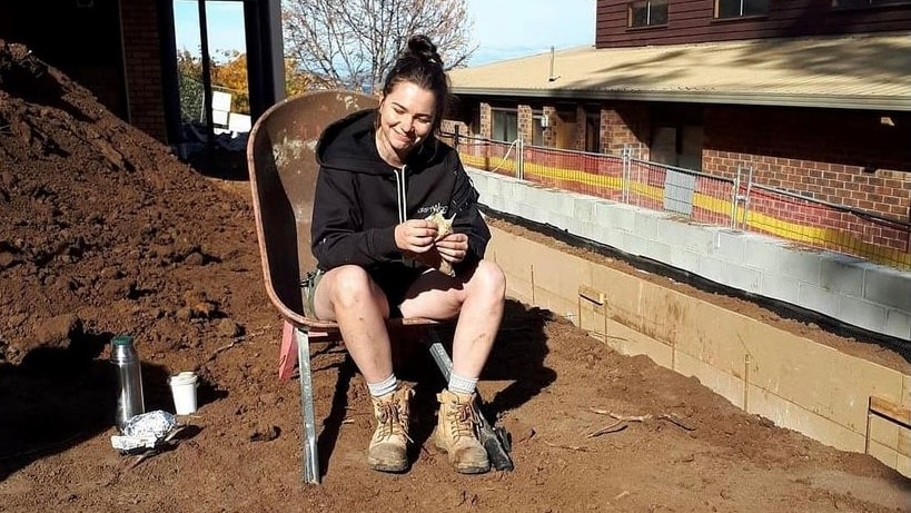 A woman sitting on a chair on dirt, in work wear