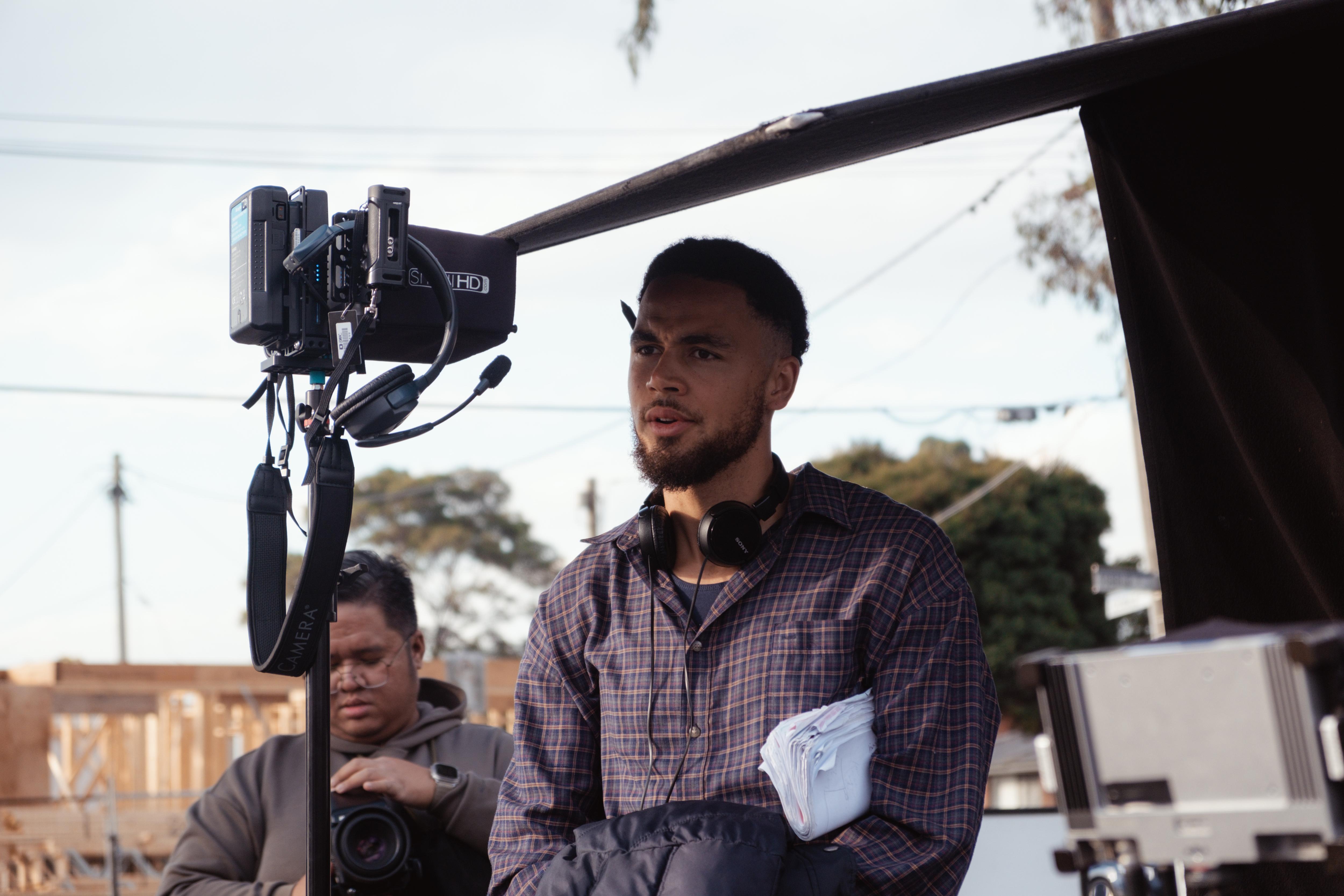 Kalu Oji, con un bolígrafo detrás de la oreja y auriculares alrededor del cuello, está de pie junto a un dispositivo de grabación.