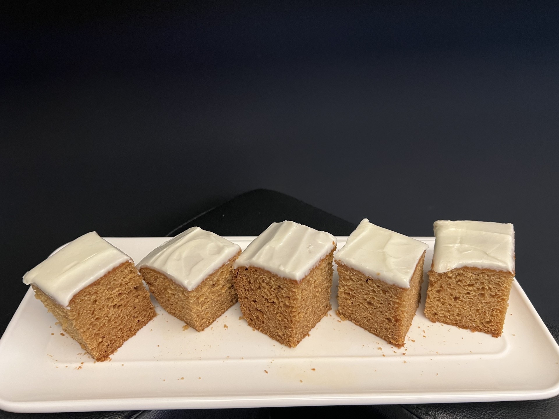 Five square slices of the ginger cake with lime icing positioned in a line on a white rectangle plate