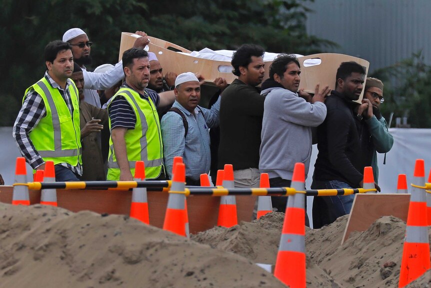 Mourners carry a wooden open-topped casket for a funeral.