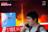 A man, speaking on a mobile phone, watches a news report detailing a North Korea missile launch.