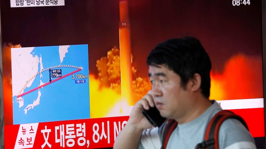 A man, speaking on a mobile phone, watches a news report detailing a North Korea missile launch.