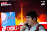 A man, speaking on a mobile phone, watches a news report detailing a North Korea missile launch.