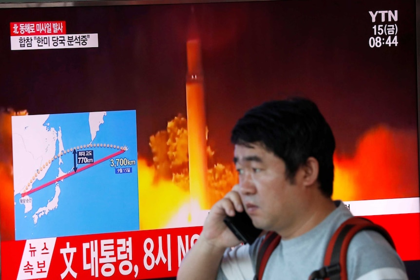 A man, speaking on a mobile phone, watches a news report detailing a North Korea missile launch.