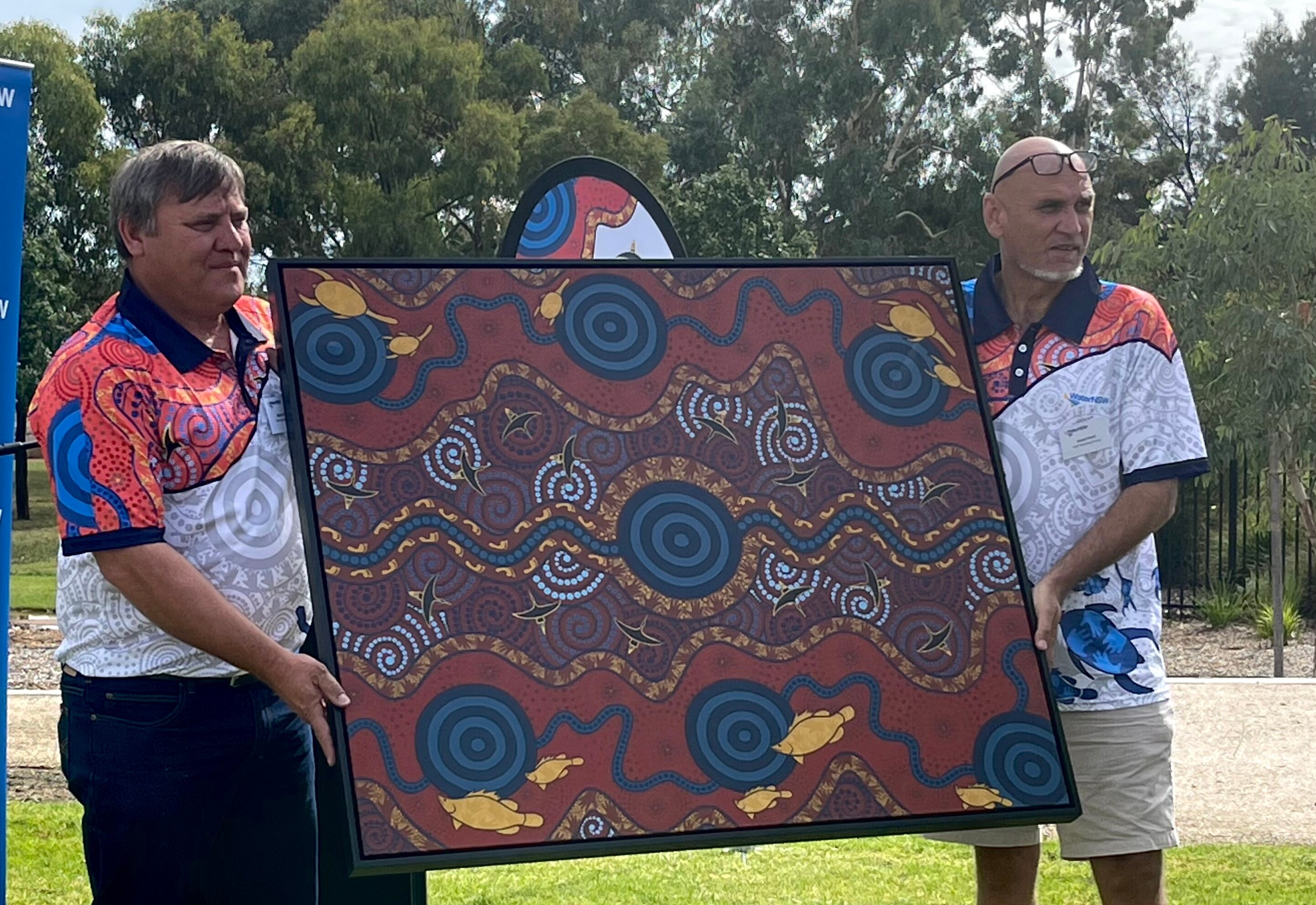 Two men hold a canvas painted with Indigenous symbols for water.