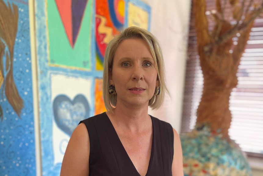 A woman wearing a black dress stands in front of colourful artwork