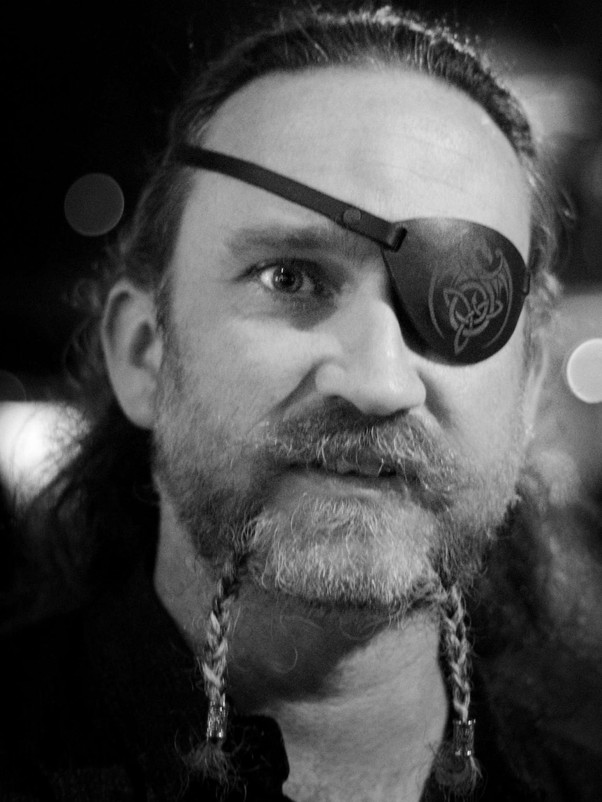 A black and white photo of a man with an eye patch and a braided bread.