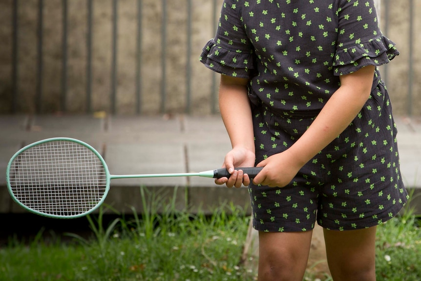 A ten-year-old girl is seen over her father's shoulder holding a badminton racquet. 
