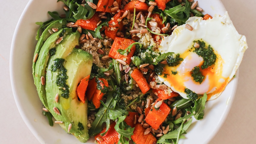 Chopped roasted carrots in a salad with quinoa, avocado, fried egg and green herby sauce.