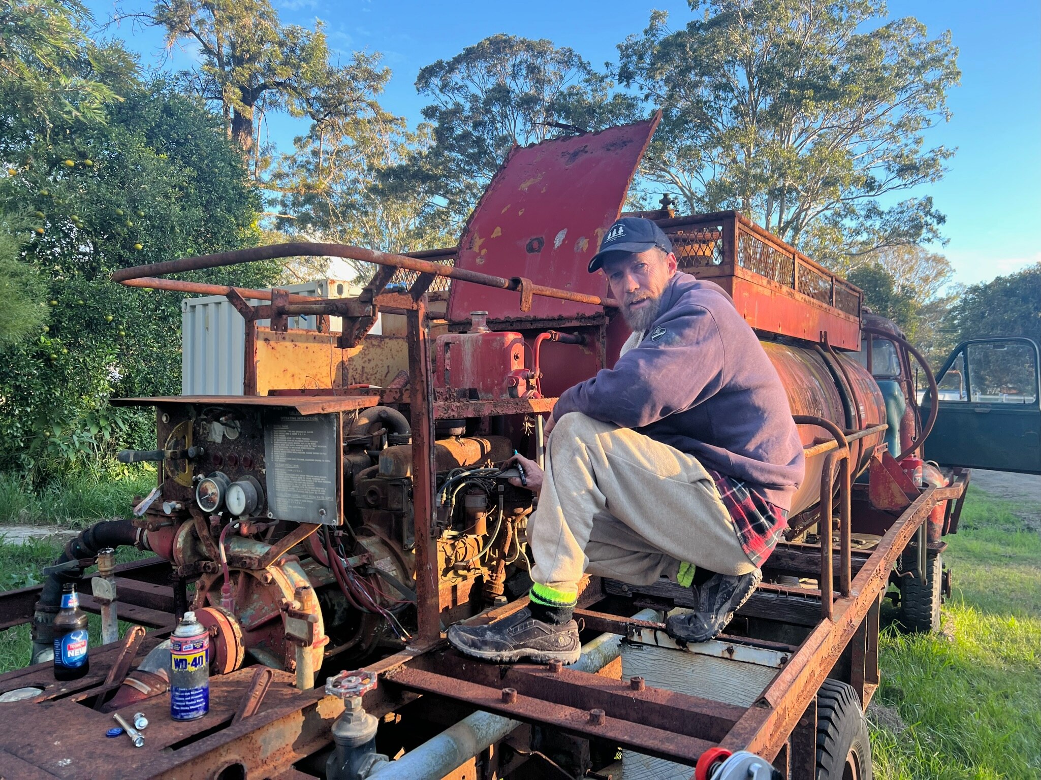 A man crouched near an old engine at the back of the old fire truck.