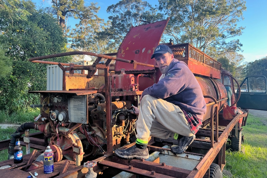 A man crouched near an old engine at the back of the old fire truck.