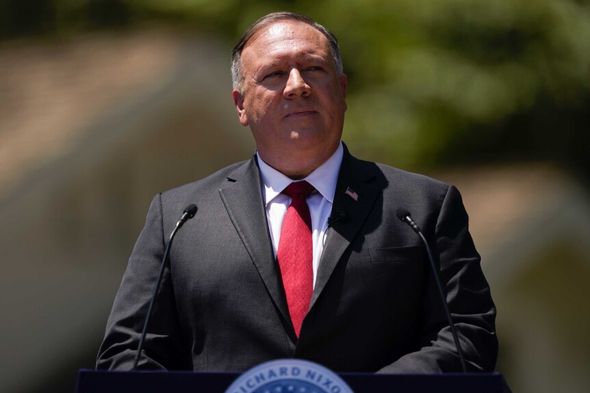 Mike Pompeo stands at a lectern while giving a speech. He's wearing a black suit and a red tie