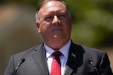 Mike Pompeo stands at a lectern while giving a speech. He's wearing a black suit and a red tie