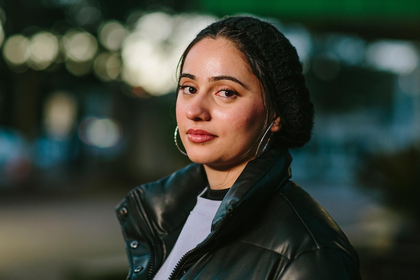 Young Muslim woman Jasmine Joyan wearing black beanie and puffer jacket looking to the side.