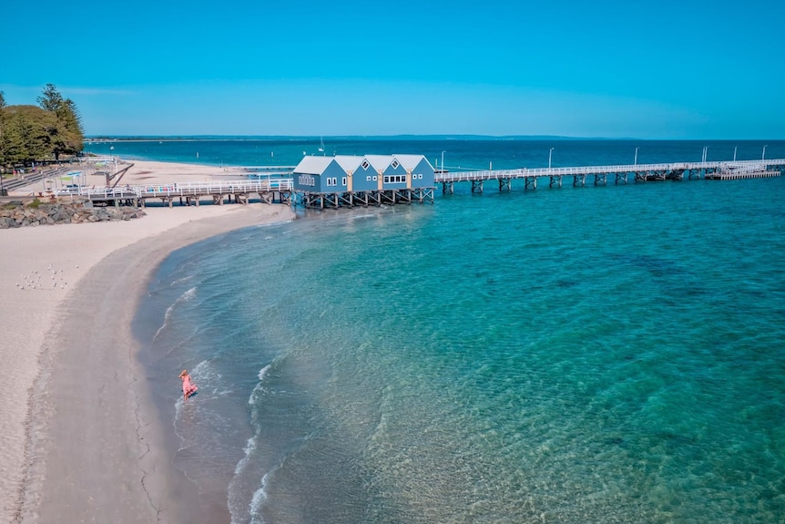 Clear ocean water and a beach with Busselton jetty in the background.