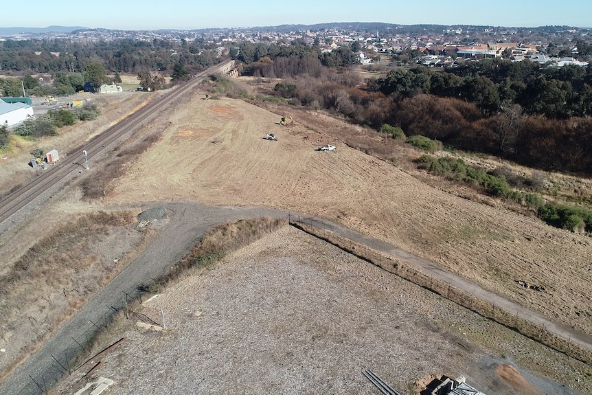 An aerial view looking down onto an empty paddock next to the train line with Goulburn city in the background.