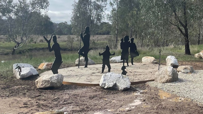 eight black silhouettes of people standing in circle with rocks around them