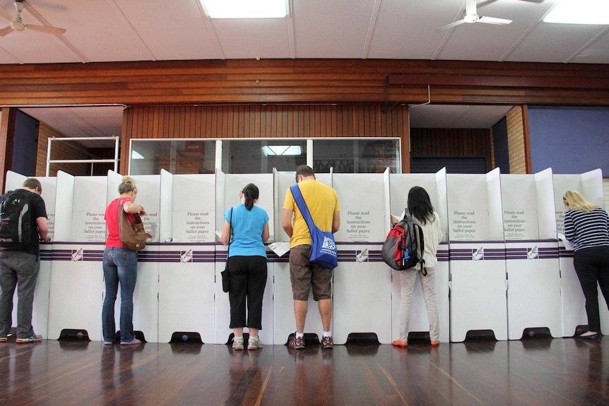 A row of people fill out forms at a polling booths during the Federal election.