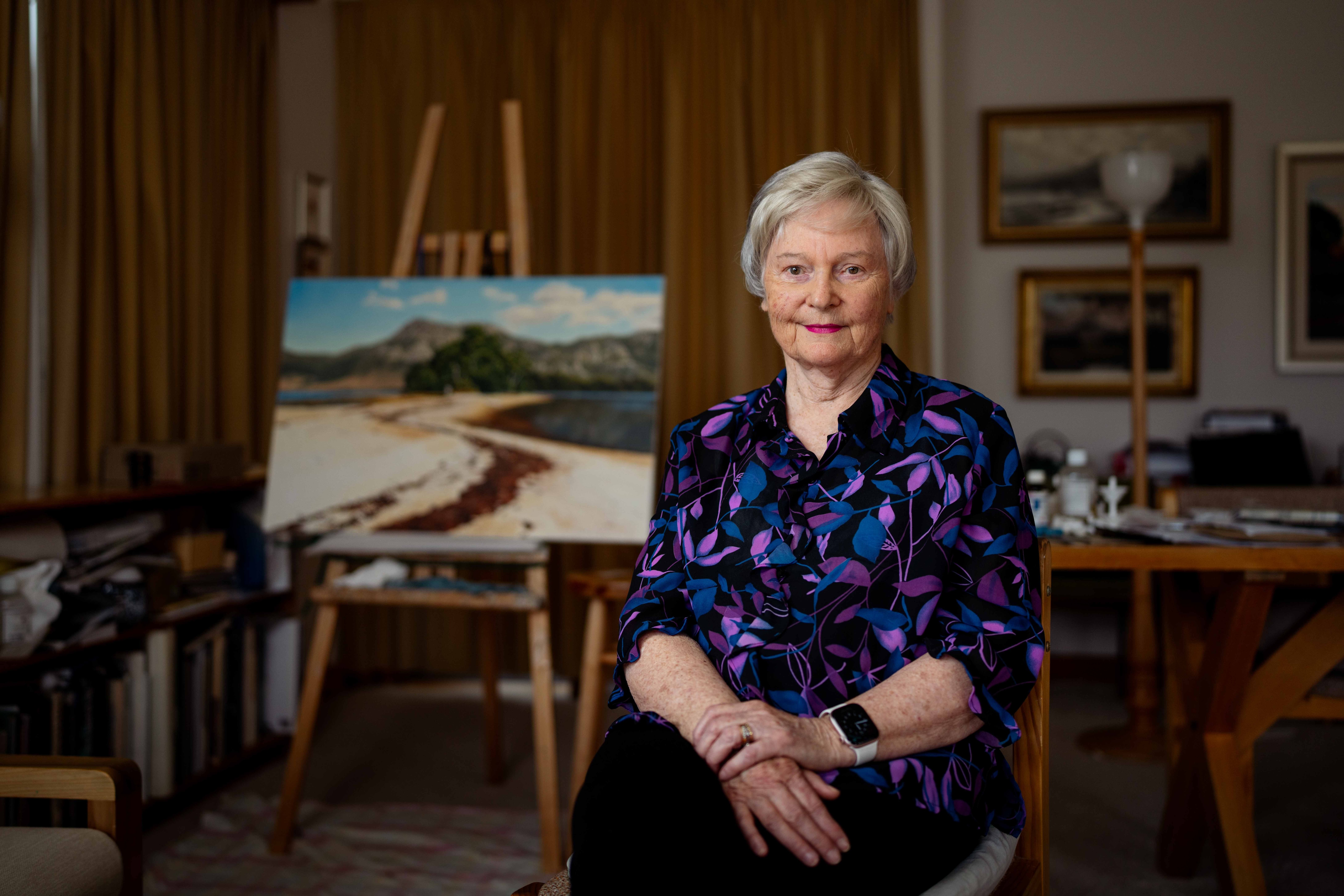 Mujer sonriendo para una foto y sentada frente a un cuadro.